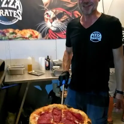 A Pizza Pirates crew member holding a pizza in front of the pirate-cat banner