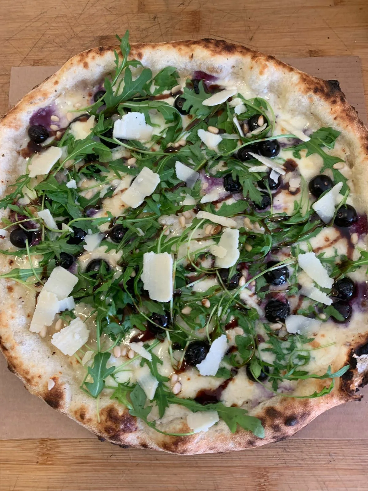 Pizza topped with rocket, dark olives and shaved cheese