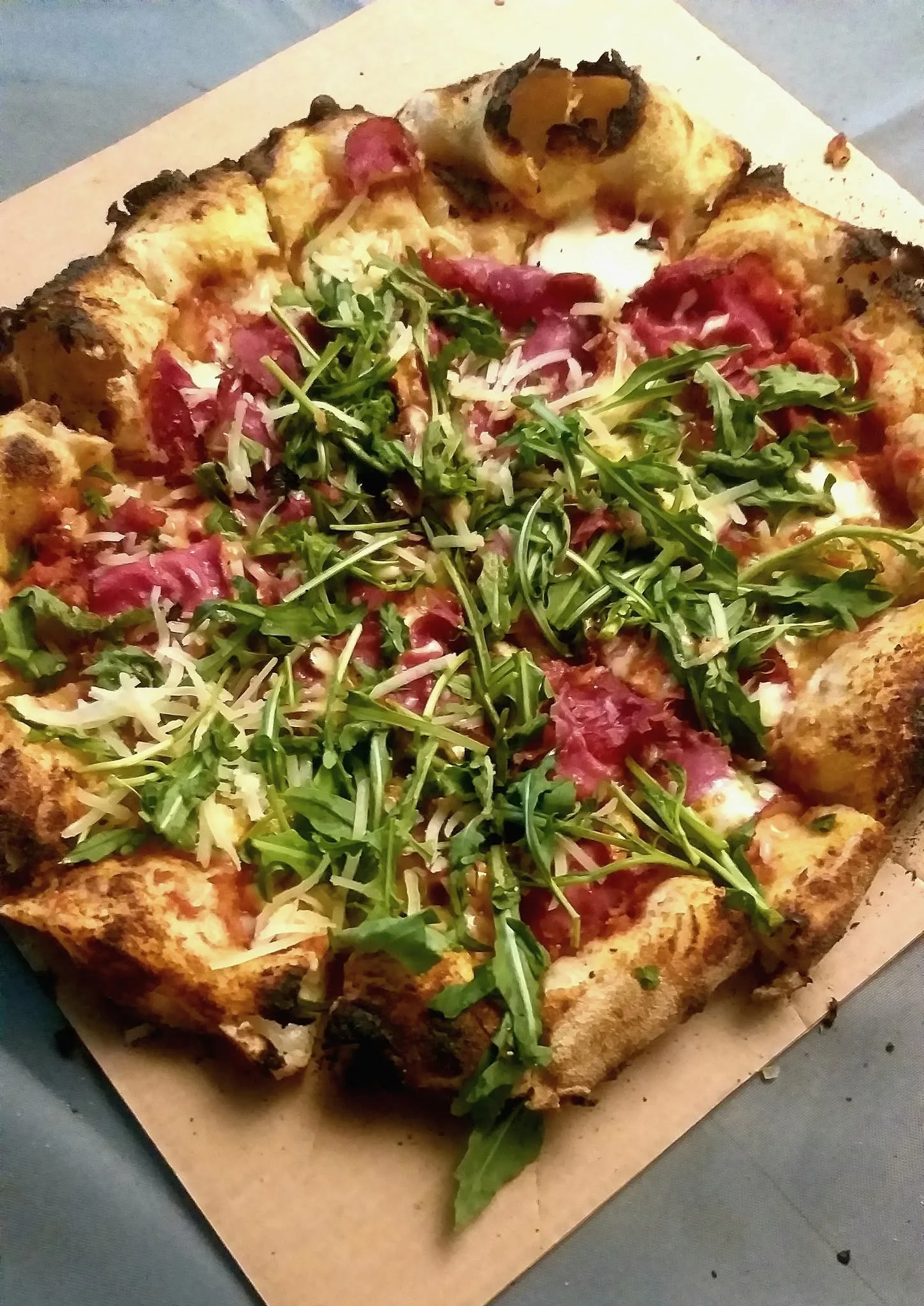 Pizza topped with rocket, cured meat and grated cheese
